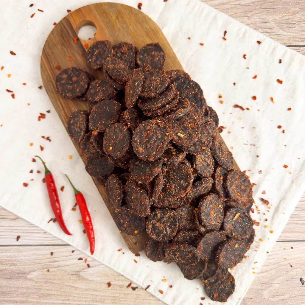 Chilli biltong wheels small on a wood cutting board showing a pile of biltong wheels main image